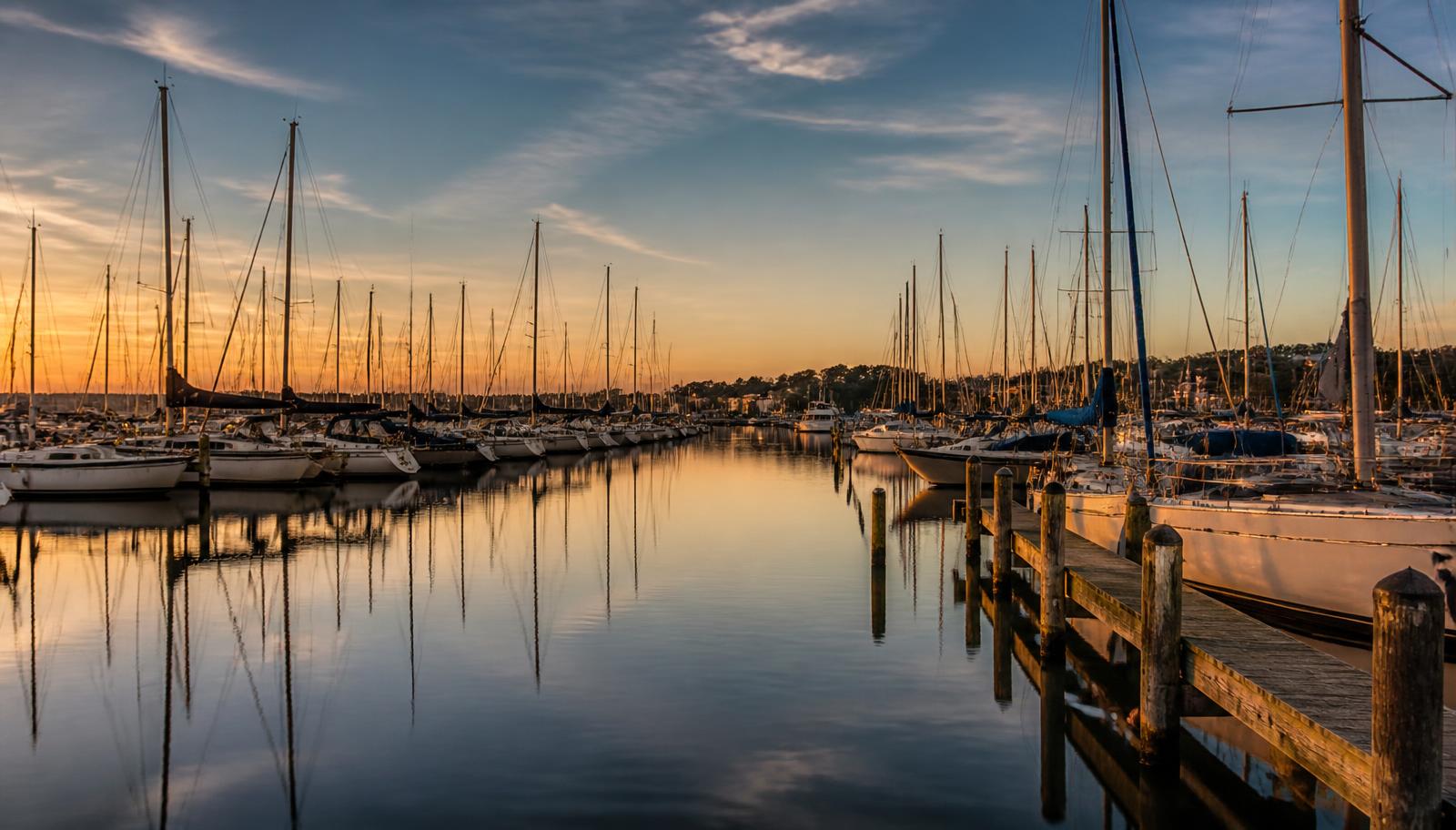 Sailboat masts reflected in a calm marina at golden hour
